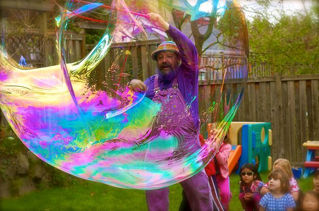 A huge rainbow bubble drifting over children in a garden