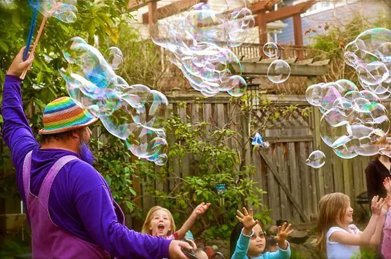 Garry in purple overalls sending bubbles over kids